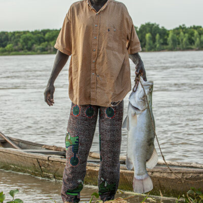  André Bénamour- Pêche à la ligne au fil de l'eau sur le fleuve Niger - Niger, 2006 - Autres techniques, la pêche à la ligne au fil de l’eau, on laisse traîner derrière une embarcation une ligne qui permet quelquefois de grosses prises, comme ici sur cette photo où Moussa le pêcheur est assez fier de la capture de ce capitaine.